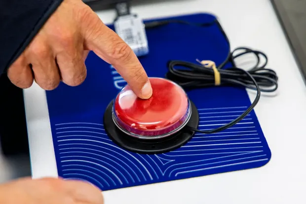 Mão de um utilizador a pressionar um botão acessível vermelho ligado a um PC